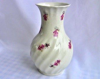 Può includere: Un vaso in ceramica bianca con un design a spirale e accenti floreali rosa.