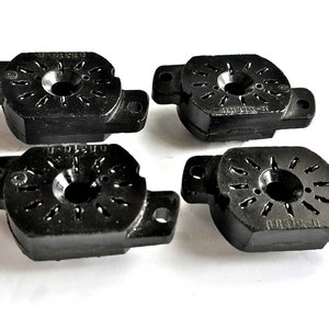 Puede incluir: Cuatro componentes eléctricos de plástico negro con un agujero circular en el centro y una serie de pequeños agujeros alrededor del borde. Cada componente tiene el texto "11-01EU" impreso en él.