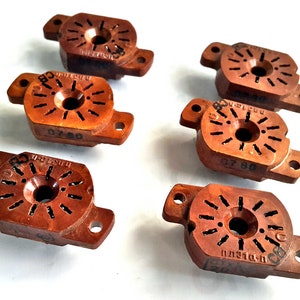 Puede incluir: Seis componentes eléctricos de plástico marrón con un centro circular y múltiples agujeros alrededor del borde. Cada componente tiene un número impreso, como "07 60".