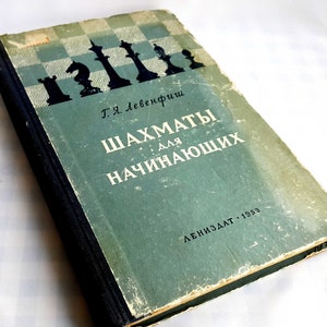 Puede incluir: Un libro verde vintage titulado "Шахматы для начинающих" (Ajedrez para principiantes) de Т.Я. Лебедевич. La portada del libro presenta un tablero de ajedrez blanco y negro con piezas de ajedrez en silueta.
