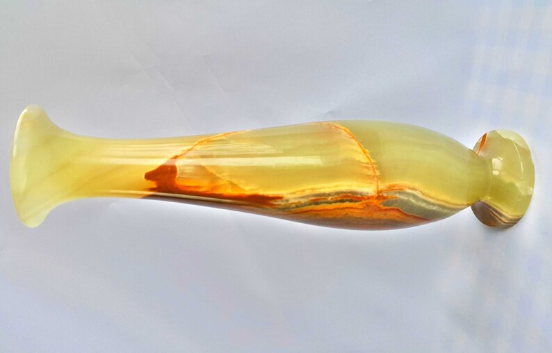 Pu&ograve; includere: Un vaso lungo e sottile in onice verde e arancio. Il vaso ha un'ampia apertura e una base stretta.