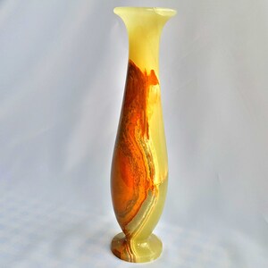 Pu&ograve; includere: Un vaso alto e sottile in onice verde, arancione e marrone. Il vaso ha un'ampia apertura e una base stretta.
