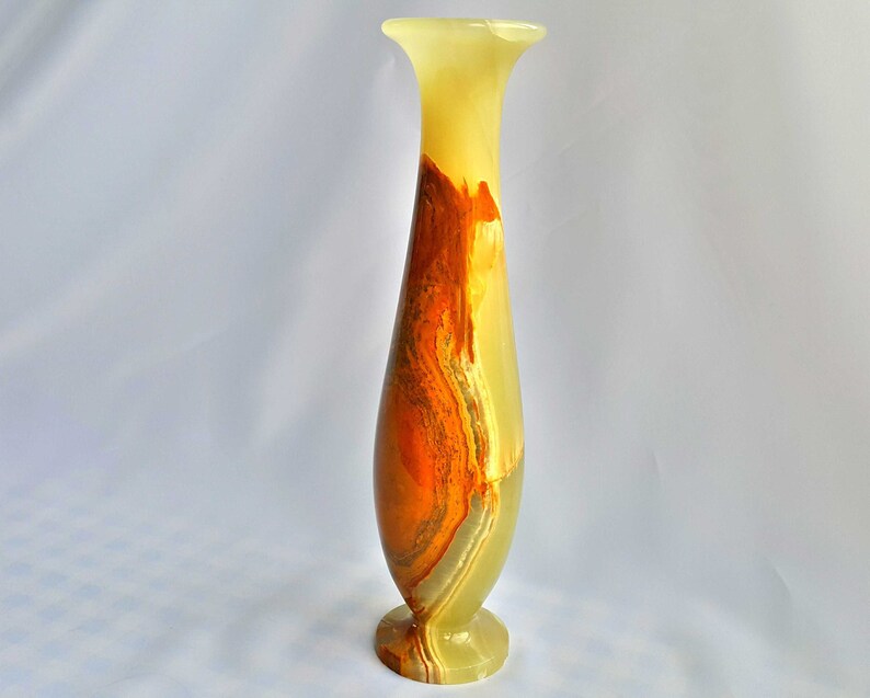 Pu&ograve; includere: Un vaso alto e sottile in onice verde, arancione e marrone. Il vaso ha un'ampia apertura e una base stretta.