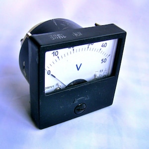 Puede incluir: Un voltímetro analógico negro con una cara blanca y una aguja que apunta a 10 voltios. El medidor tiene una caja de plástico negro y una cubierta de plástico transparente. El medidor está etiquetado con "V" para voltios y tiene marcas de 0 a 50 voltios.
