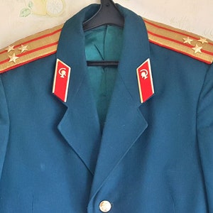 May include: A dark blue military uniform jacket with gold and red trim, three gold stars on the shoulder, and red and gold insignia on the collar.