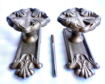 Può includere: Due maniglie per porte antiche con pomelli a forma di croce decorati e piastre decorative. Le maniglie sono in metallo e hanno una finitura argentata. Le maniglie sono fissate a una superficie bianca con viti.