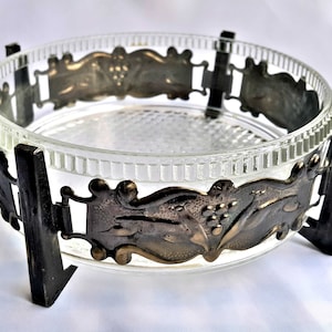 May include: A clear glass bowl with a decorative metal rim and four metal legs. The metal rim has a floral design.