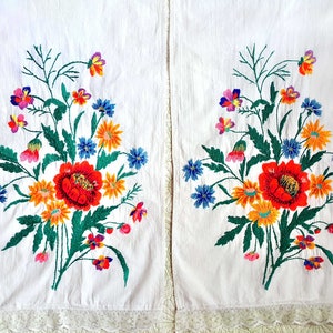 May include: Two white fabric panels with embroidered floral designs. Each panel features a bouquet of colorful flowers, including red, yellow, orange, blue, and pink. The flowers are arranged in a symmetrical pattern.