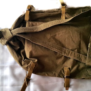 May include: A brown canvas backpack with adjustable straps. The straps are made of a brown canvas material and have metal buckles.