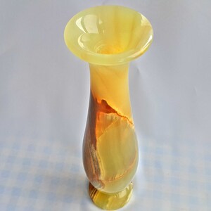 Pu&ograve; includere: Un vaso in onice giallo e marrone con un'ampia apertura e un labbro svasato. Il vaso &egrave; realizzato in pietra naturale e presenta un motivo marmoreo unico.