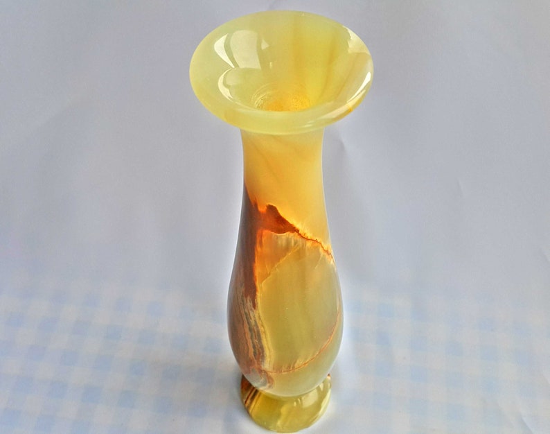 Pu&ograve; includere: Un vaso in onice giallo e marrone con un'ampia apertura e un labbro svasato. Il vaso &egrave; realizzato in pietra naturale e presenta un motivo marmoreo unico.