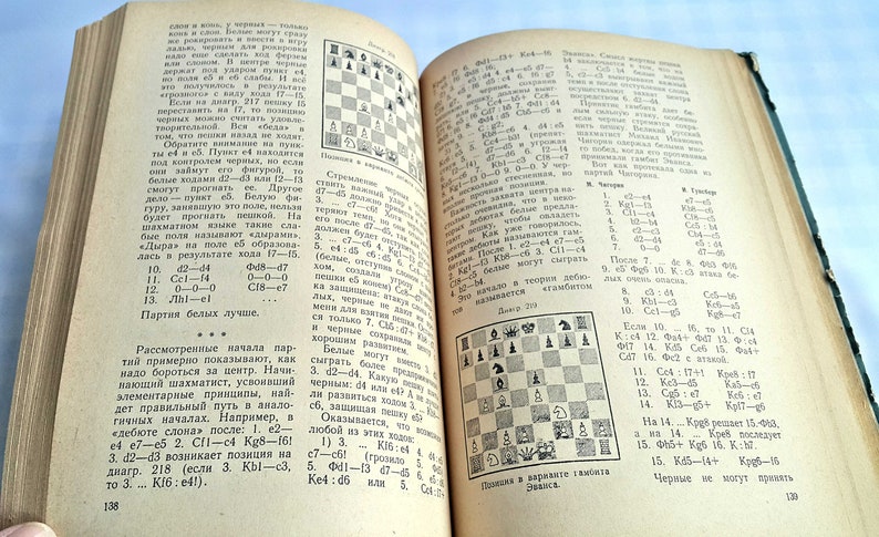 May include: A black and white chessboard with pieces set up for a game. The board is on a page from a book with text in Russian. The text discusses chess strategy and tactics.