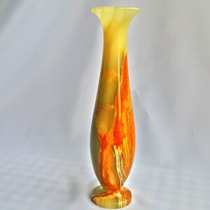 Pu&ograve; includere: Un vaso alto e sottile in onice verde e arancio. Il vaso ha un'ampia apertura e una base stretta.