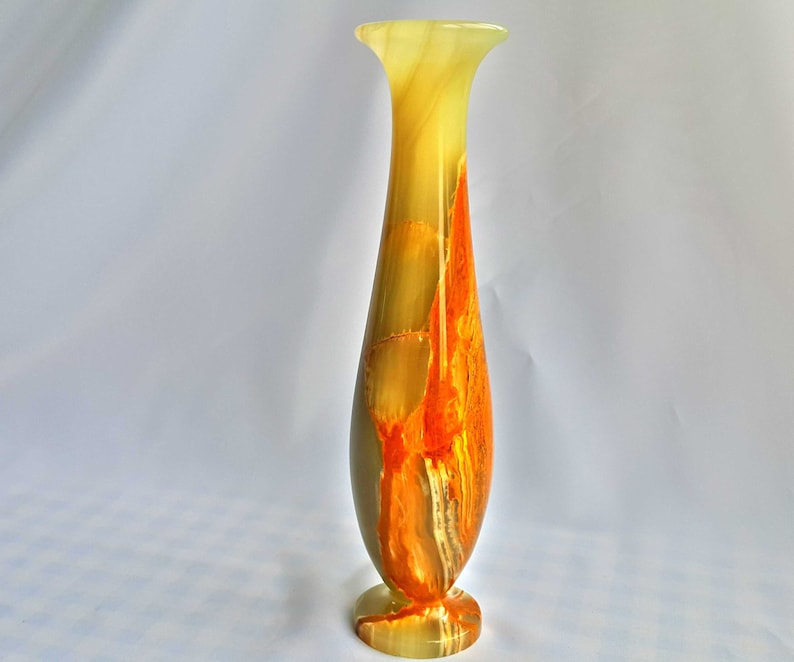Pu&ograve; includere: Un vaso alto e sottile in onice verde e arancio. Il vaso ha un'ampia apertura e una base stretta.