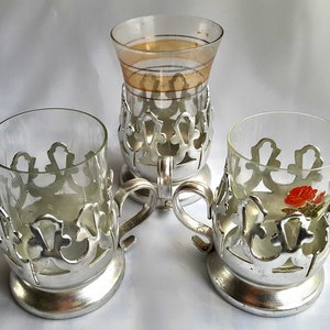 Peut inclure: Trois supports en argent pour verres à thé avec des verres en verre transparent. Deux des verres ont un motif floral et un autre est uni.