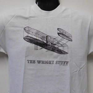 May include: White t-shirt with a black and white illustration of the Wright Flyer airplane and the text "The Wright Stuff".