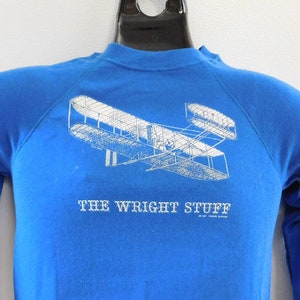May include: A blue sweatshirt with a white graphic of an airplane and the text "THE WRIGHT STUFF".