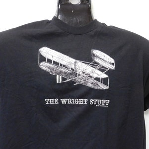 May include: Black t-shirt with a white graphic of the Wright brothers' airplane and the text "The Wright Stuff".