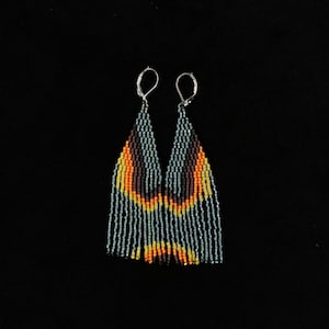 Könnte beinhalten: Ein Paar Perlenohrringe mit Fransenmuster. Die Ohrringe weisen ein Muster aus orangefarbenen, gelben und braunen Perlen mit hellblauem Hintergrund auf. Die Ohrringe hängen an silberfarbenen Ohrhaken.