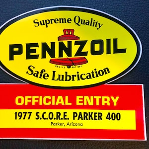 May include: A yellow and red sticker with the text "Supreme Quality PENNZOIL Safe Lubrication REG US PAT OFF OFFICIAL ENTRY 1977 S.C.O.R.E. PARKER 400 Parker, Arizona"