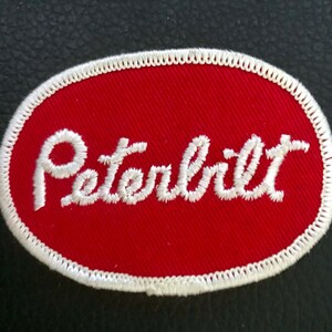 May include: White embroidered "Peterbilt" logo on a red oval patch.