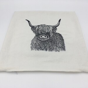May include: A white canvas pillow with a black and white line drawing of a Highland cow with long horns.