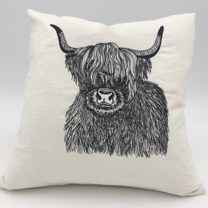 May include: A white pillow with a black and white line drawing of a Highland cow with long, shaggy hair.