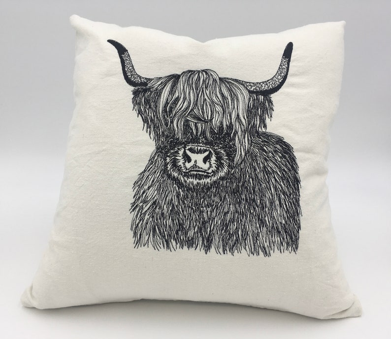 May include: A white pillow with a black and white line drawing of a Highland cow with long, shaggy hair.