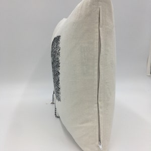 May include: A white linen pillow with a black and white embroidered design of a tree. The pillow has a zipper closure on the side.