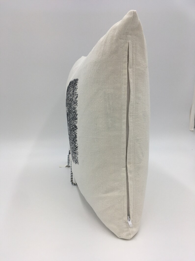 May include: A white linen pillow with a black and white embroidered design of a tree. The pillow has a zipper closure on the side.