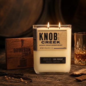 May include: A rectangular glass candle with two wicks, featuring a label that reads Knob Creek Kentucky Straight Bourbon Whiskey 100 Proof 50% Alc./Vol. Small Batch. Beside it is a wooden box labeled Bourbon Candle Co. with a candle illustration.