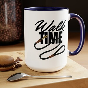 May include: White ceramic coffee mug with a blue rim and handle. The mug has a black graphic of a dog leash with the text "Walk Time" in black.