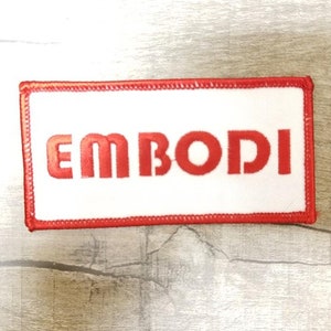 May include: Red embroidered patch with white background and the word "EMBODI" in red lettering.