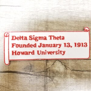 Op de afbeelding: Witte patch met rode tekst die "Delta Sigma Theta Founded January 13, 1913 Howard University" luidt. De patch is gevormd als een rol.