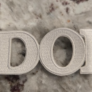 May include: White embroidered patch with the letters "DOI" in a bold, blocky font.