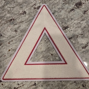 May include: A white triangular warning sign with a red border and a smaller red triangle inside. The sign has a white background and a red border.
