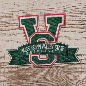Peut inclure: Patch brodé vert et blanc avec un contour rouge de la lettre "V" et le texte "Mississippi Valley State University" sur une bannière blanche.
