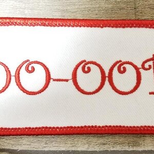 May include: White embroidered patch with a red border. The patch says "OO-OOP" in red cursive lettering.