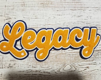 May include: A yellow felt patch with blue outlining, spelling out the word "Legacy" in a cursive font.