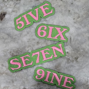 May include: Four embroidered patches with numbers spelled out in pink letters on a green background. The patches read "5IVE", "6IX", "SE7EN", and "9INE". The patches are likely for clothing or accessories.