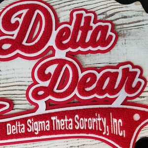 May include: Red and white felt applique with the text "Delta Dear" and "Delta Sigma Theta Sorority, Inc."