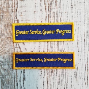 May include: Two blue fabric patches with yellow borders and the text "Greater Service, Greater Progress" in yellow embroidery.