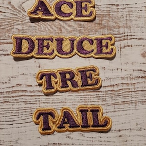May include: Four embroidered patches with the words "ACE", "DEUCE", "TRE", and "TAIL" in purple lettering on a gold background.