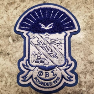 May include: Blue and white embroidered patch with a crest featuring a book, a hand reaching out, and a bird in flight. The crest is surrounded by a white banner with the text "ΦΒΣ FOUNDED 1914".