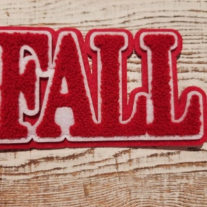 May include: Red felt "FALL" patch with white outline. The patch is made of a fuzzy material and has a slightly raised texture.