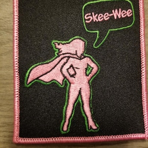 May include: Pink and green embroidered patch featuring a superhero figure and a speech bubble that says "Skee-Wee".