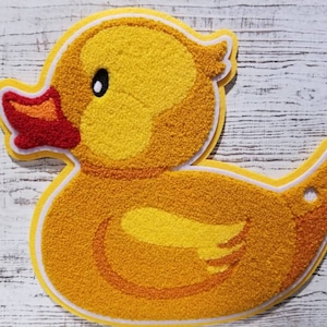 May include: A yellow rubber duck with a red beak and white eyes. The duck is made of a soft, fuzzy material.