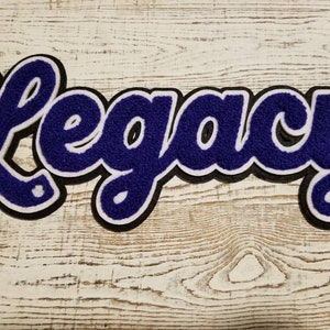 May include: Purple felt "Legacy" lettering with white outline and black backing. The letters are in a cursive font.