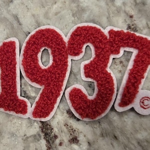 May include: Red felt patch with the number 1937 in white outlined letters. The patch has a white border.