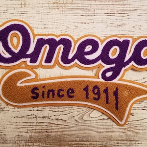 May include: Purple and white felt patch with the word "Omega" in a cursive font. Below the word is a gold felt banner with the text "Since 1911".